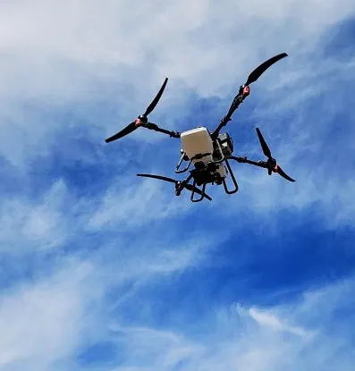 A FlyEMM agricultural spray drone in flight against a blue Iowa sky.
